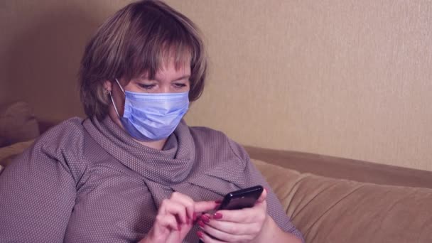 Lycklig kvinna i en mask håller en smartphone i handen, väljer en produkt — Stockvideo