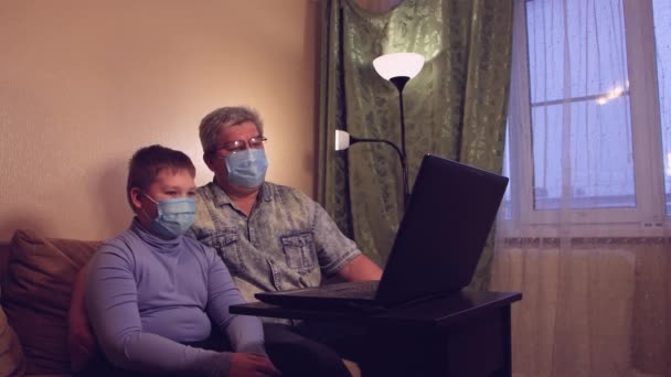 De jongen en zijn vader met maskers praten thuis online en zwaaien met hun handen.. — Stockvideo