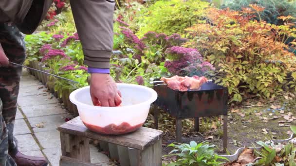 Mãos masculinas esticam pedaços de carne em um espeto em um jardim com flores — Vídeo de Stock