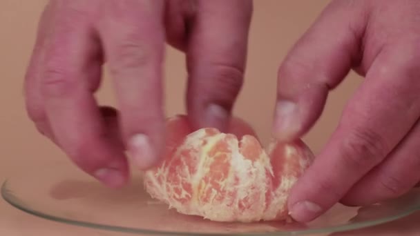 Крупным планом мужские руки отделяют очищенные кусочки мандарина на тарелке. — стоковое видео