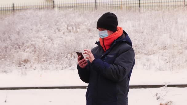 Um homem com uma máscara médica faz compras online em um smartphone — Vídeo de Stock