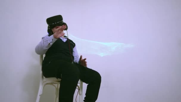 Een jongen in augmented reality bril zit op een stoel en danst vrolijk. — Stockvideo