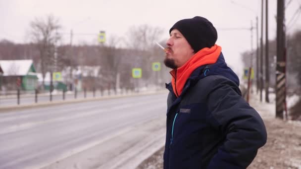 Een man met een baard steekt een sigaret aan, kijkt naar de naderende auto 's. — Stockvideo