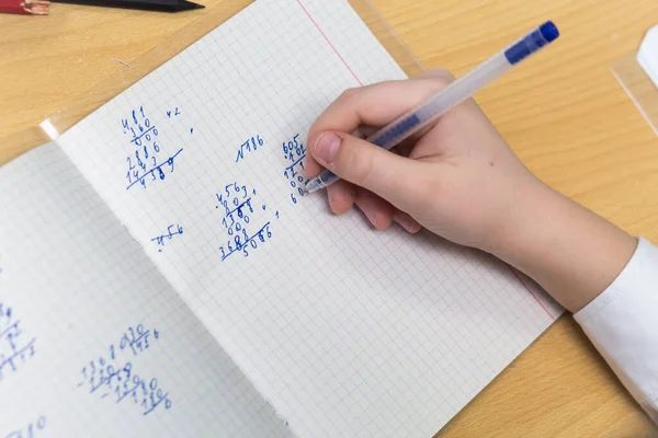 Рука девушки с перьевой ручкой с голубыми чернилами решает примеры в математике — стоковое фото