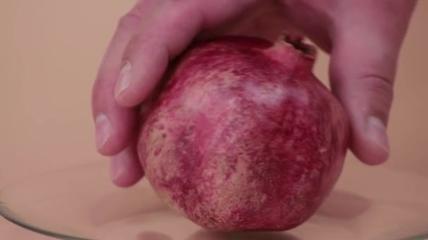 Close-up male hands lay and rotate a red pomegranate on a transparent plate. — Stockvideo