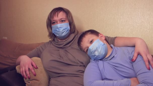 Lycklig mamma med sin son på soffan tittar på TV-filmer i medicinska masker. — Stockvideo