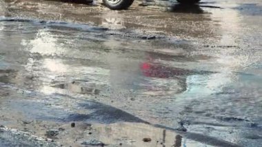 Arabalar kötü, engebeli bir yolda delikleri, çamurlu su birikintileri ve çatlakları olan.