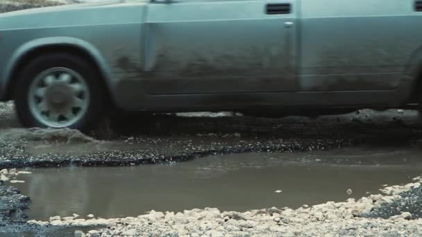 Carros mover-se lentamente em close-up em uma estrada com poças enlameadas e poços. — Vídeo de Stock