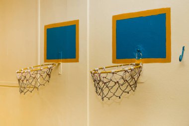 Spor salonundaki sarı duvarda asılı iki eski basketbol potası..