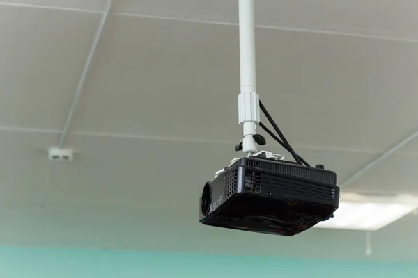 Černý videoprojektor je zavěšen na dlouhé konzole pod stropem. — Stock fotografie