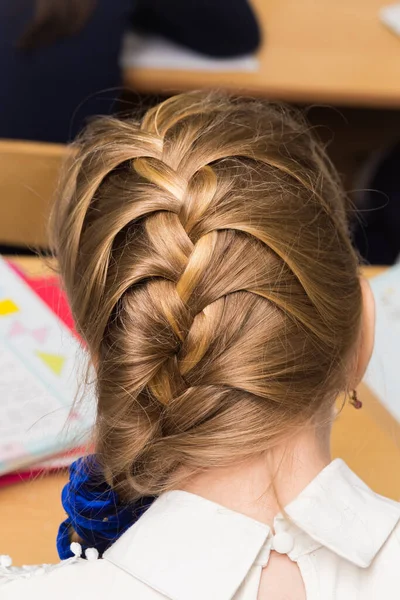 Girls hairstyle braided in a braid fixed with a blue elastic band close-up.