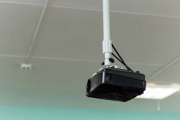 The black video projector is suspended from a long bracket under the ceiling. Royalty Free Stock Photos