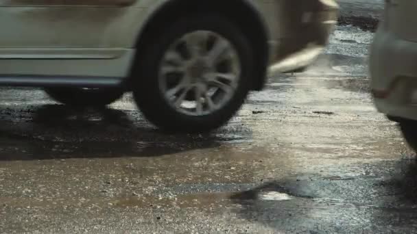 Auto 's rijden langzaam over een slechte weg met gaten, modderige plassen en scheuren. — Stockvideo