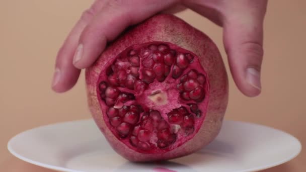Mannelijke handen close-up tonen een ronde snede van een rode granaatappel op een witte plaat. — Stockvideo