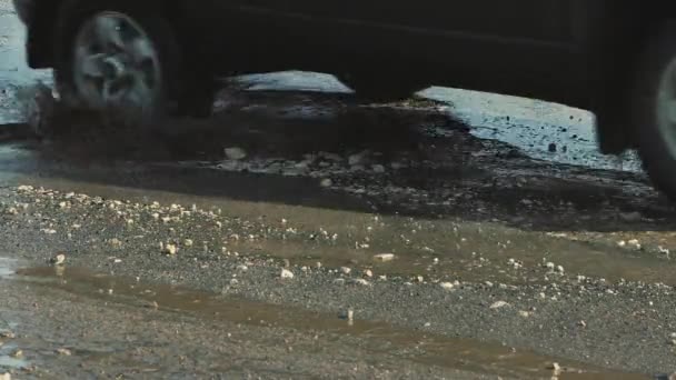 Машины крупным планом едут по плохой дороге с дырами, грязными лужицами и трещинами. — стоковое видео