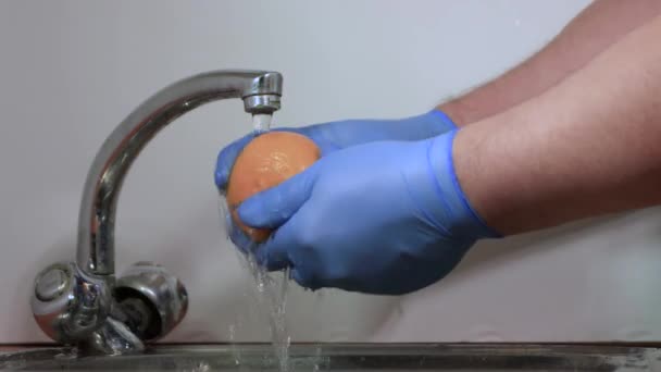 Las manos masculinas en guantes close-up lavan la mandarina anaranjada bajo el agua corriente. — Vídeos de Stock
