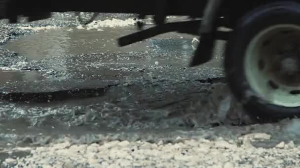 Langzame auto rijden close-up op een slechte weg met scheuren, modderige plassen en putten. — Stockvideo