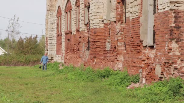 Мужчина в джинсовой рубашке ходит по разрушенному зданию. — стоковое видео