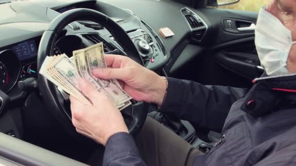 A happy man in a mask sitting behind the wheel is counting dollars close-up — Stock Video