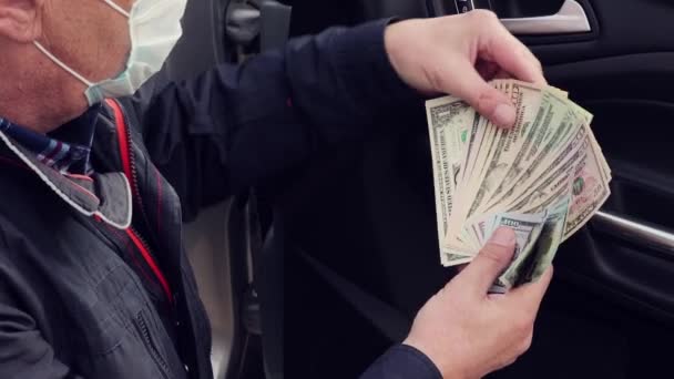 En man i mask sitter på tröskeln till bilen räknar dollar närbild. — Stockvideo