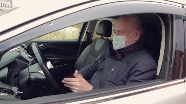 Um homem de negócios com uma máscara, dirigindo um carro, faz uma entrada em um caderno. — Vídeo de Stock