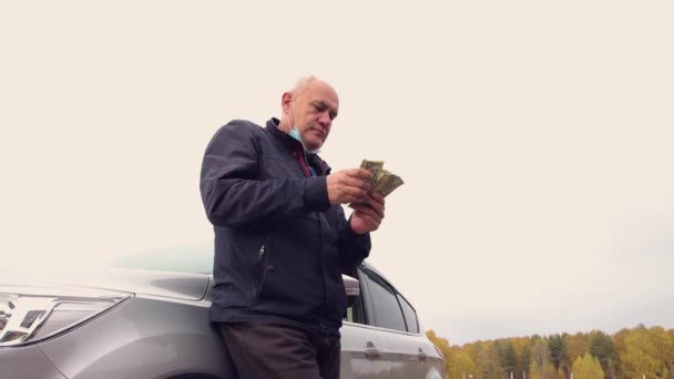 Ein glücklicher Mann, der am Auto steht, zählt Dollar - sein Einkommen. — Stockvideo