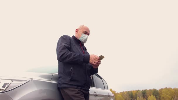 車のそばに立っているマスクのビジネスマンは、ドルを数えている-彼の収入 — ストック動画