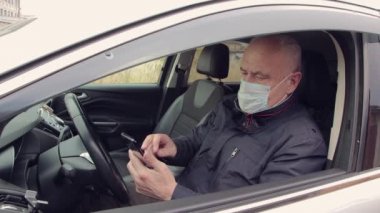 Maskeli bir iş adamı, araba kullanıyor, akıllı bir telefonla çalışıyor.. 