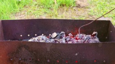 Bir adam ızgarada yanan kırmızı kömürleri karıştırmak için demiri kullanır.. 