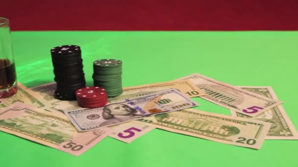На зеленому ігровому столі є доларові купюри, фішки казино і келих віскі — стокове відео