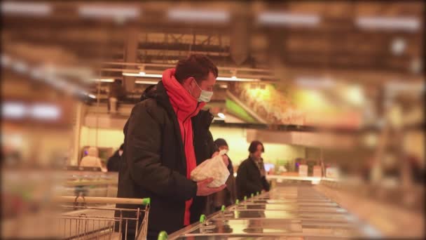 En mand i en butik inspicerer frossen mad, med en maske på hans ansigt. – Stock-video