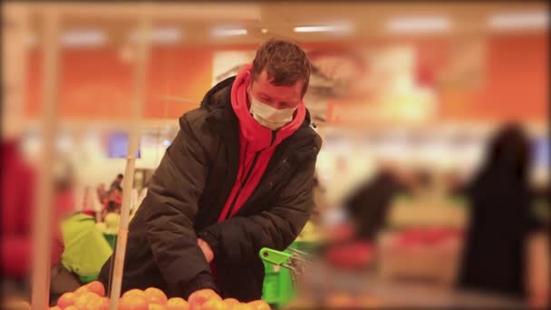 슈퍼마켓에서 트롤리를 하고 있는 남자가 얼굴에 가면을쓴 사과를 집는다 — 비디오