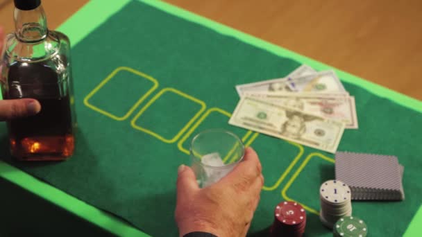Close-up shot of a gamblers hand pouring whiskey into a glass with ice. — Stock Video