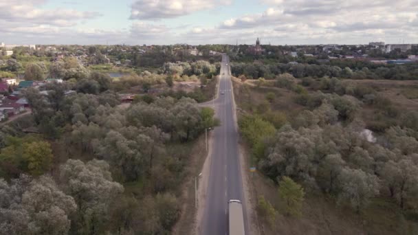 Volare su una piccola strada con auto, alberi verdi e città in lontananza. — Video Stock