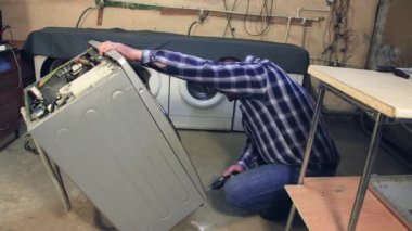 Adam çamaşır makinesinin altındaki vidaları söküyor..