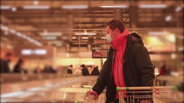 슈퍼마켓에서 트롤리를 하고 있는 남자가 얼굴에 마스크를 쓴 채 가격을 보고 있습니다. — 비디오