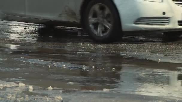 Voitures conduisent en gros plan sur une mauvaise route cahoteuse avec des fosses et des flaques. — Video