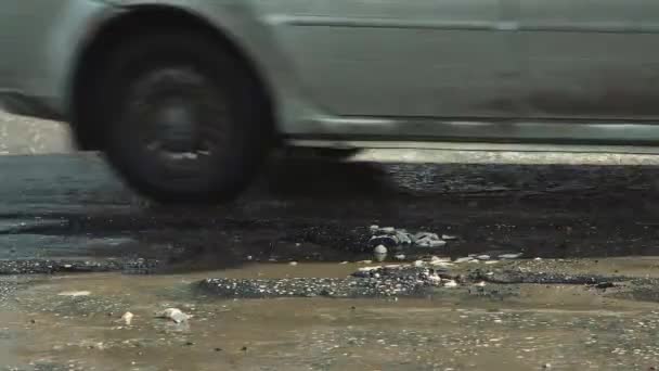 Nahaufnahme von Autorädern auf einer kaputten Straße mit Gruben und Pfützen. — Stockvideo