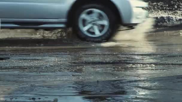 De wielen van auto 's rijden op een slechte weg met gaten, modderige plassen en scheuren. — Stockvideo