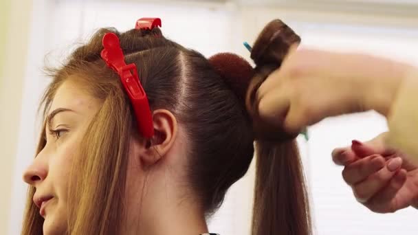 Handen krullen een haarlok met een haarspeld, een meisje in een schoonheidssalon. — Stockvideo