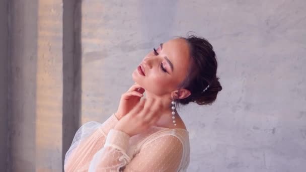 Een meisje in een witte jurk poseert voor een fotograaf, houdt haar handen bij haar nek. — Stockvideo