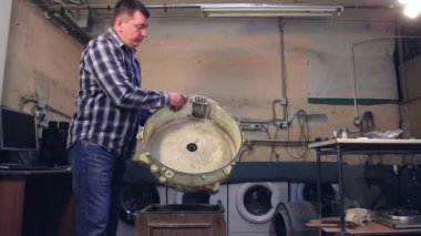 Usta çamaşır makinesinin varilini söker ve gösterir..
