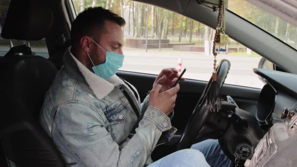 Un joven moderno con una máscara médica, conduciendo, trabajando por teléfono. — Vídeo de stock