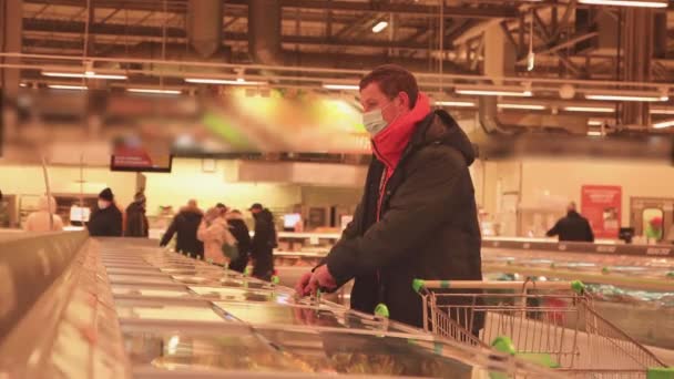 Egy férfi a szupermarketben egy kirakatot vizsgál, maszkkal az arcán.. — Stock videók