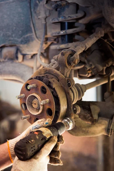 Male hands in gloves use a power tool to clean rust on the wheel hub of a car. Stock Image