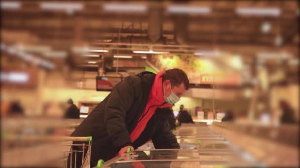Ein Mann in einem Geschäft holt mit einer Maske im Gesicht Lebensmittel aus dem Kühlschrank — Stockvideo