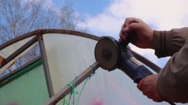 Öğütücüyle erkek eli, mavi gökyüzüne karşı paslı metal bir yapı kesiyor..