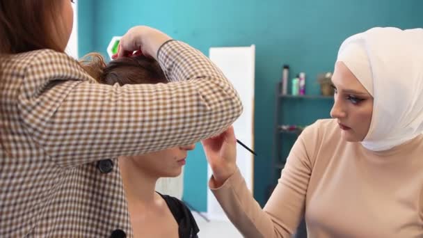 Das Mädchen lässt sich von zwei Meistern die Wimpern färben und die Haare stylen. — Stockvideo