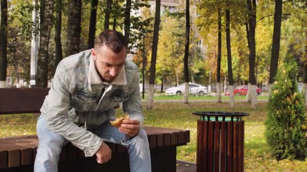 現代の若い男は貪欲においしいハンバーガーを食べる. — ストック動画