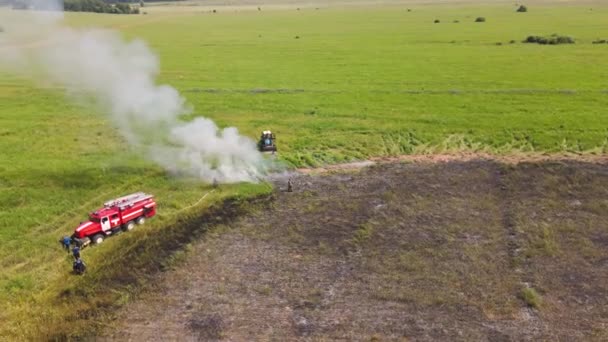 Ein Feuerwehrauto und ein Traktor am Rande eines abgebrannten Feldes mit Rauch. — Stockvideo